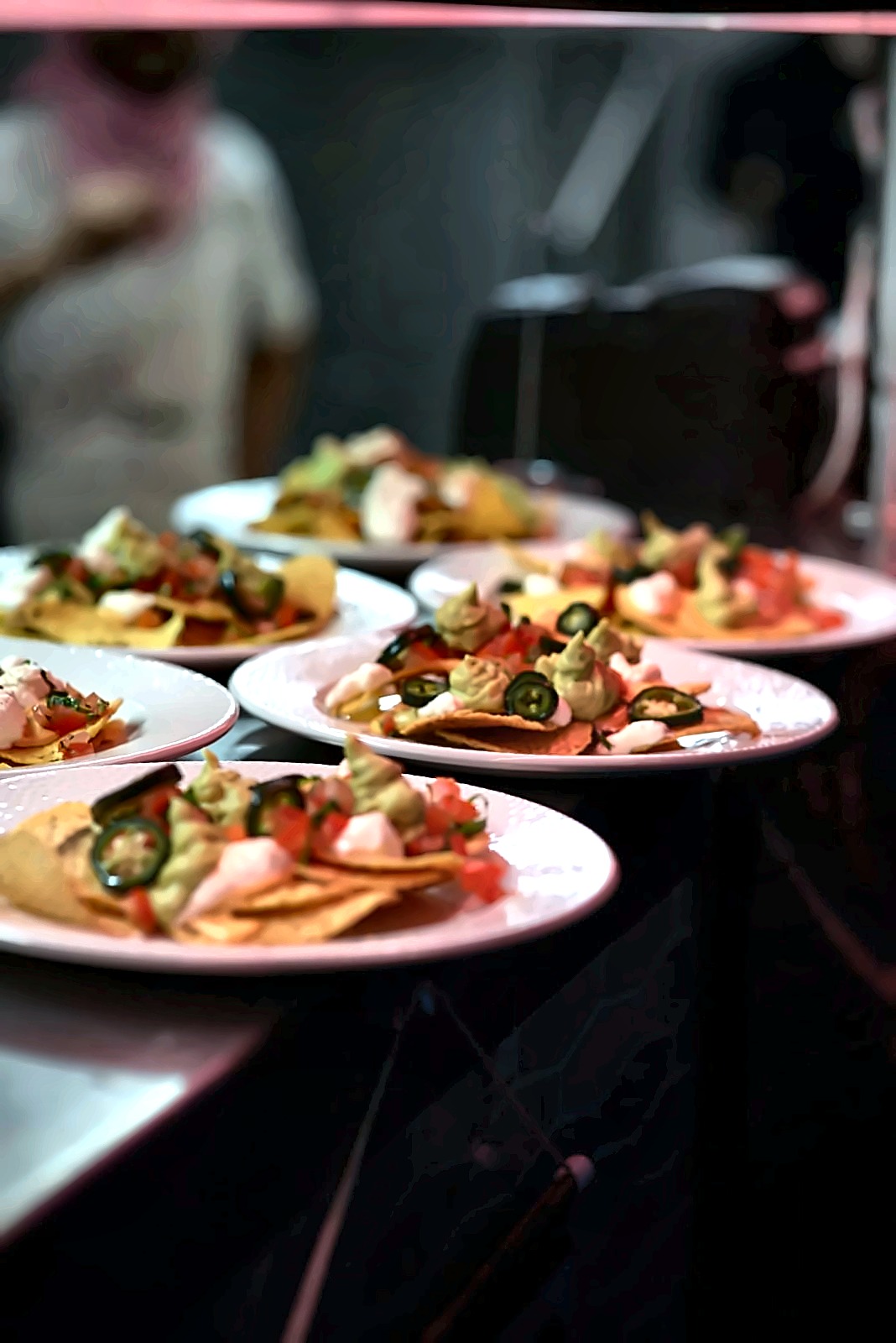 Loaded nachos with jalapenos, salsa and crema on pink plates